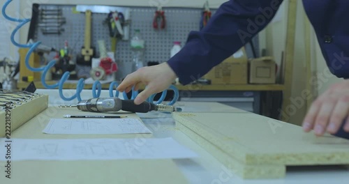 A furniture maker or furniture designer in blue workwear marking and preparing particle board parts on a workbench in a furniture factory workshop.