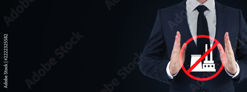 Businessman showing stop gesture beside prohibited factory symbol on dark background with generous copy space for industrial safety concept design.