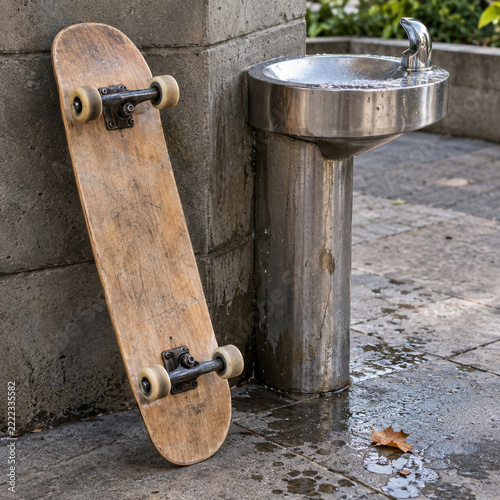 A worn skateboard beside a public drinking fountain