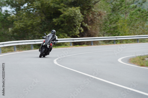 biker on a sport motorcycle rides fast while leaning on a turn on a winding road, motion blur highlighting the dynamic action, close-up