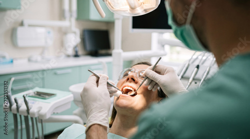 Female patient wearing safety glasses undergoing dental cleaning while dentist works beside equipment