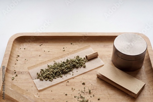 Overhead shot of ground cannabis flower on rolling paper with a filter tip, next to a metal grinder and paper pack on a bamboo tray, ready for a joint.