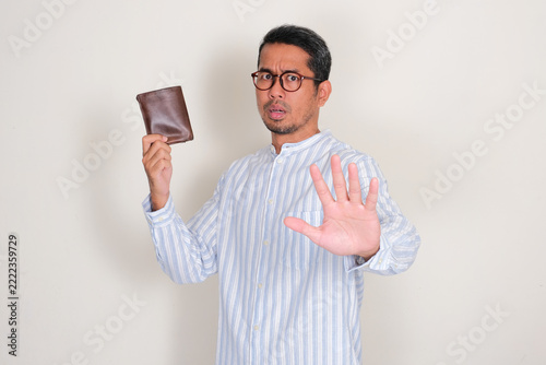 Adult Asian man holding a wallet and doing stop hand gesture with serious expression