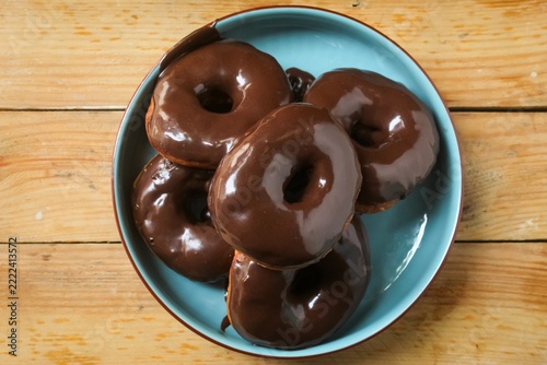 several chocolate donuts on a plate on a wooden table