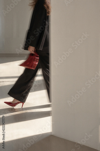 Woman Walking in Red High Heels with a Matching Handbag in a Minimalist Sunlit Interior