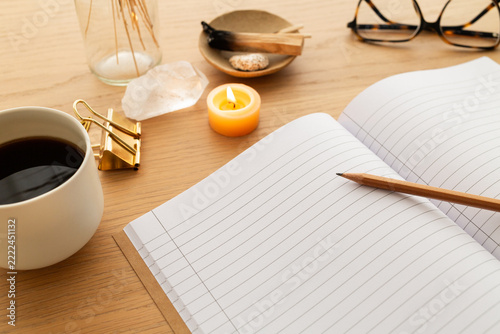Scène d'écriture, gros plan sur un cahier ouvert, une bougie allumée, du palo santo et une tasse de café