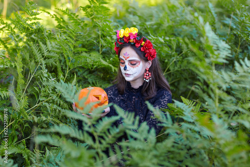 Halloween beauty portrait of female among ferns looking at Halloween pumpkin in hand.