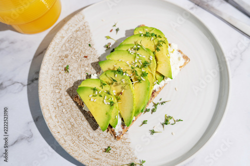 Sunlit breakfast plate with avocado cress crispbread and citrus juice.