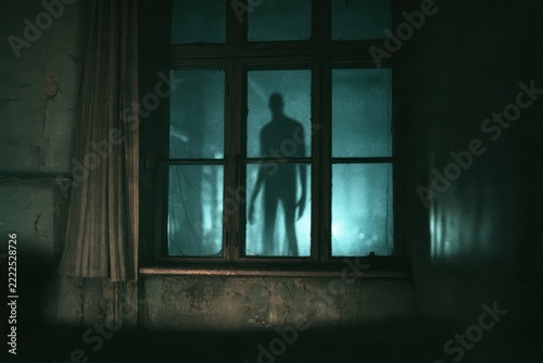 Creepy shadow figure standing outside a window in a dark, abandoned room