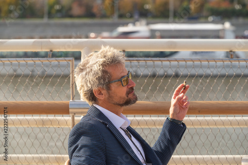 Senior man in eyeglasses smoking cigarette outdoors in city