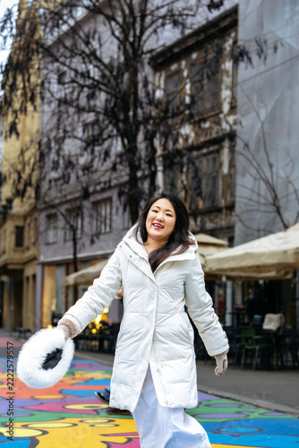 Japanese woman in white winter coat holding a fluffy wreath on a colorful painted city street in winter urban setting, Christmas advent 