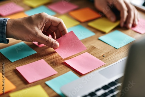 Hands arranging colorful sticky notes on a wooden desk during a team brainstorming session.