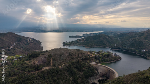 Epic aerial view of Los Molinos dam, reservoir lake and sun rays shining through clouds in Cordoba
