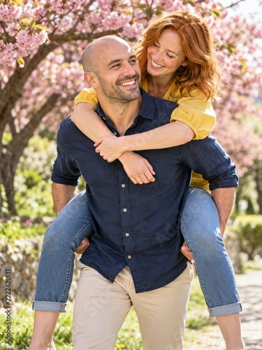 Smiling Man Giving a Woman a Piggyback Ride under Pink Blossoms