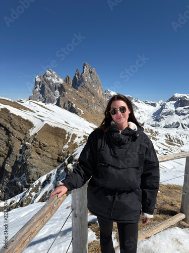 A woman stands near snowy mountains in the Dolomites of Italy, enjoying winter hiking and the adventure of solo travel.