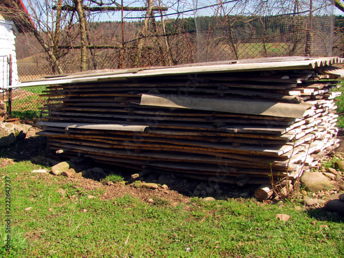 Stacked raw wooden planks air drying naturally outdoors near a rural workshop