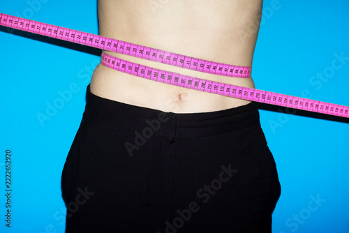 Pink measurement tape around waist against blue background
