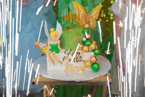Creative custom dessert prepared for a magical kids birthday party celebration. Beautiful fairy themed birthday cake decorated with green buttercream, gold spheres, and a topper.