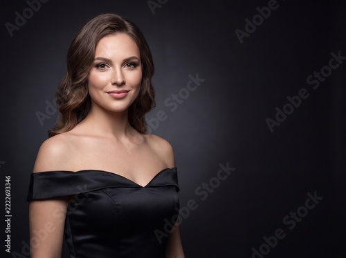 Model poses in black dress against dark background
