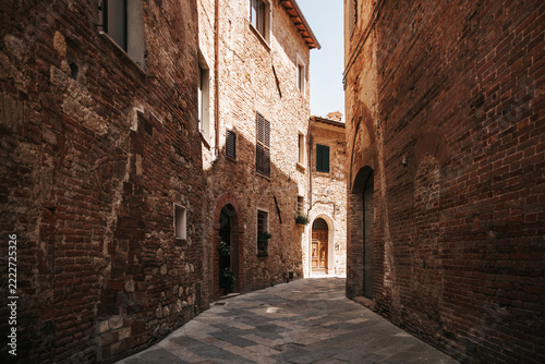Empty narrow medieval street in the historic center of Montepulciano, Tuscany, Italy. Traditional brick and stone buildings along a picturesque old alley with sunlight and shadows.