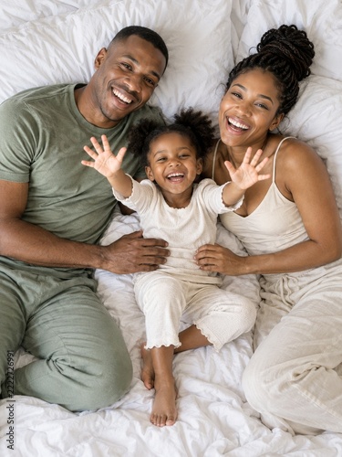 Overhead Portrait of Laughing Parents and Daughter on White Bedding