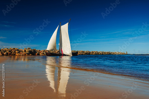 A sailboat with white sails in the beach of the Baltic sea