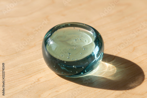 Smooth blue-green glass paperweight on pale maple surface in sunlight