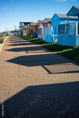Pretty wooden beach huts along Tankerton promenade in Whitstable, Kent, UK. The low but bright autumn casts deep shadows of the huts on the walkway.
