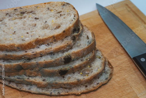 rotten bread pieces exhibiting fungal mold growth stay arranged on wooden cutting board near chef knife. decayed multigrain loaf pieces illustrate inedible stale bakery contamination closeup.