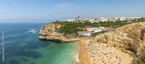 View of sandy beach with bathers, turquoise sea, Praia Benagil, rugged sandstone coastline, rock formations in the sea, Algarve, Lagos, Portugal