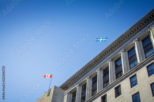 Canadian and Quebec flags above downtown Montreal buildings, on business, finance, investment and urban identity in Quebec, Canada.