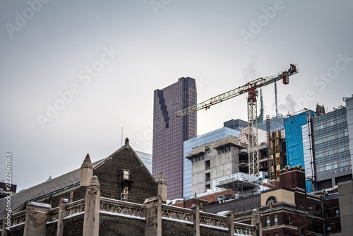Construction site in downtown Toronto, Canada, with cranes, unfinished condo structures, older brick buildings and modern high rise towers showing the city's changing real estate skyline.