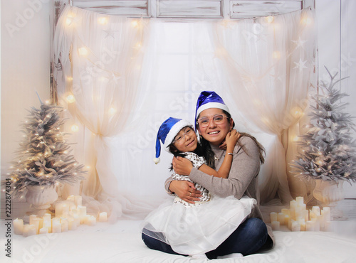Divorced single mother and her 5-year-old Latina daughter with glasses excited celebrate Christmas and New Year's together, wearing Santa hats