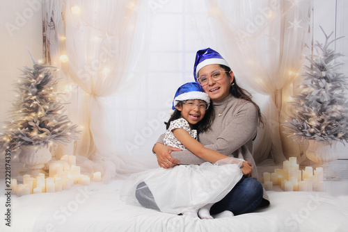Divorced single mother and her 5-year-old Latina daughter with glasses excited celebrate Christmas and New Year's together, wearing Santa hats
