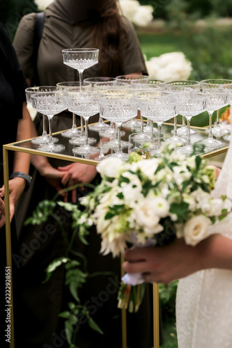 Obraz na plátně Crystal champagne coupes arranged on a gold serving tray beside a white bridal bouquet, creating an elegant wedding reception scene with floral details and refined styling