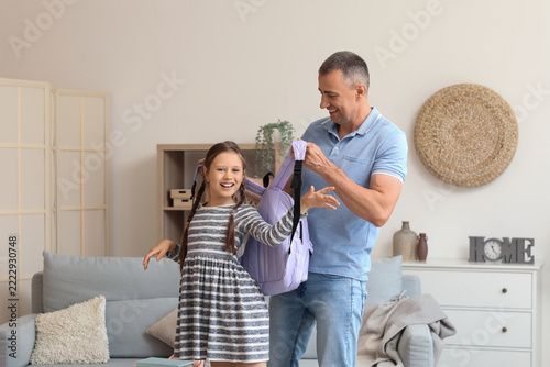 Back to school preparation, father helping daughter put on backpack for first...
