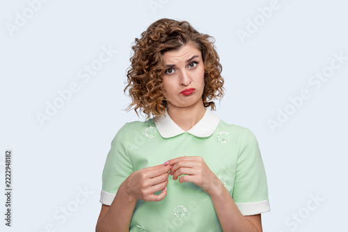 Fotografie Young woman with curly hair making a pouty face and looking at camera on a light background