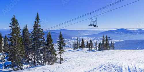 Winter panoramic view of Sheregesh ski resort in Russia. Cable car ascends above the fir conifer forest and mountain valley, with houses hotels and distant peaks below, banner scenery, Green mount.