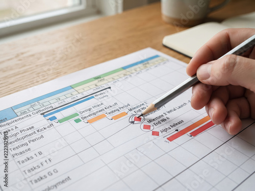 Hand reviewing and annotating project Gantt chart schedule on rustic wooden table