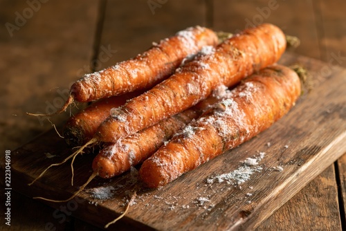 Carrots with mold on wooden surface in a kitchen setting illustrate food waste and spoilage concerns