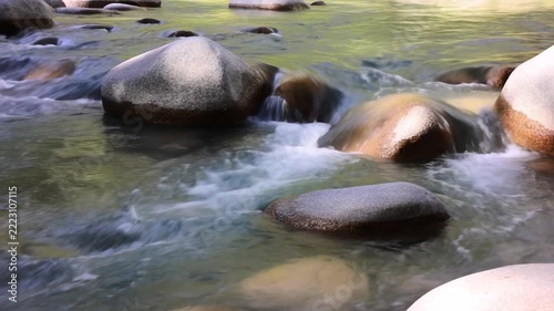 Slow motion static shot of river water flowing around smooth boulders in mountain forest stream during daytime