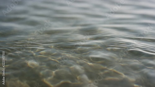 Slow motion close up of shallow water ripples flowing over pebbled seabed near shoreline at daytime