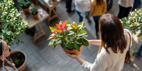 A woman holds a pot with a beautiful plant, likely a purchase from a local nursery or garden center, to add color and life to her home decor