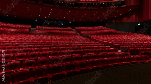 Empty red velvet theater auditorium rows seen from the stage perspective. Deep red seating. Plush fabric. Rows of seats. Dark stage foreground. Audience seating. Performance venue. Concert hall