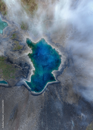 Overhead view of a blue and turquoise mountain lake with low clouds above rocky shores