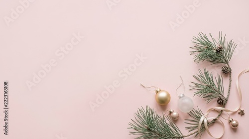 Minimalist winter holiday background showcasing a corner arrangement of pine branches, gold and frosted baubles, small pinecones, and a ribbon on a solid pastel pink surface