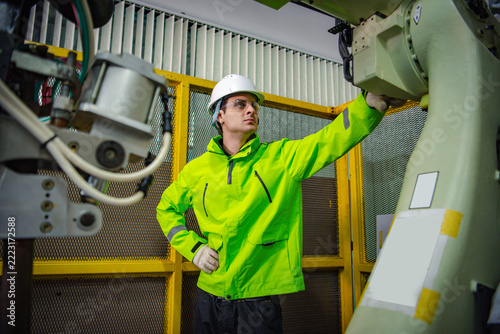 Robotic machine engineers is checking the operation of a robot arm manufacturing machine and welding robots in a production process at an industrial factory.