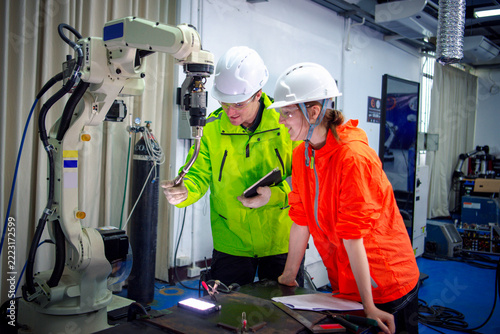 Team of Robotic machine  engineers checking the operation of a robot arm manufacturing machine and welding robots in a production process at an industrial factory.