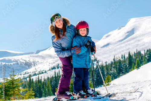 Sporty woman teach skiing child boy at mountains alpine winter resort.Young mother,coach,trainer learn little son kid riding downhill,family,enjoy extreme sport activities recreation