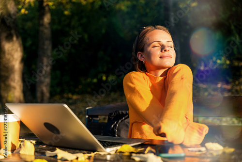 Woman enjoying nature in cozy autumn park while working on laptop